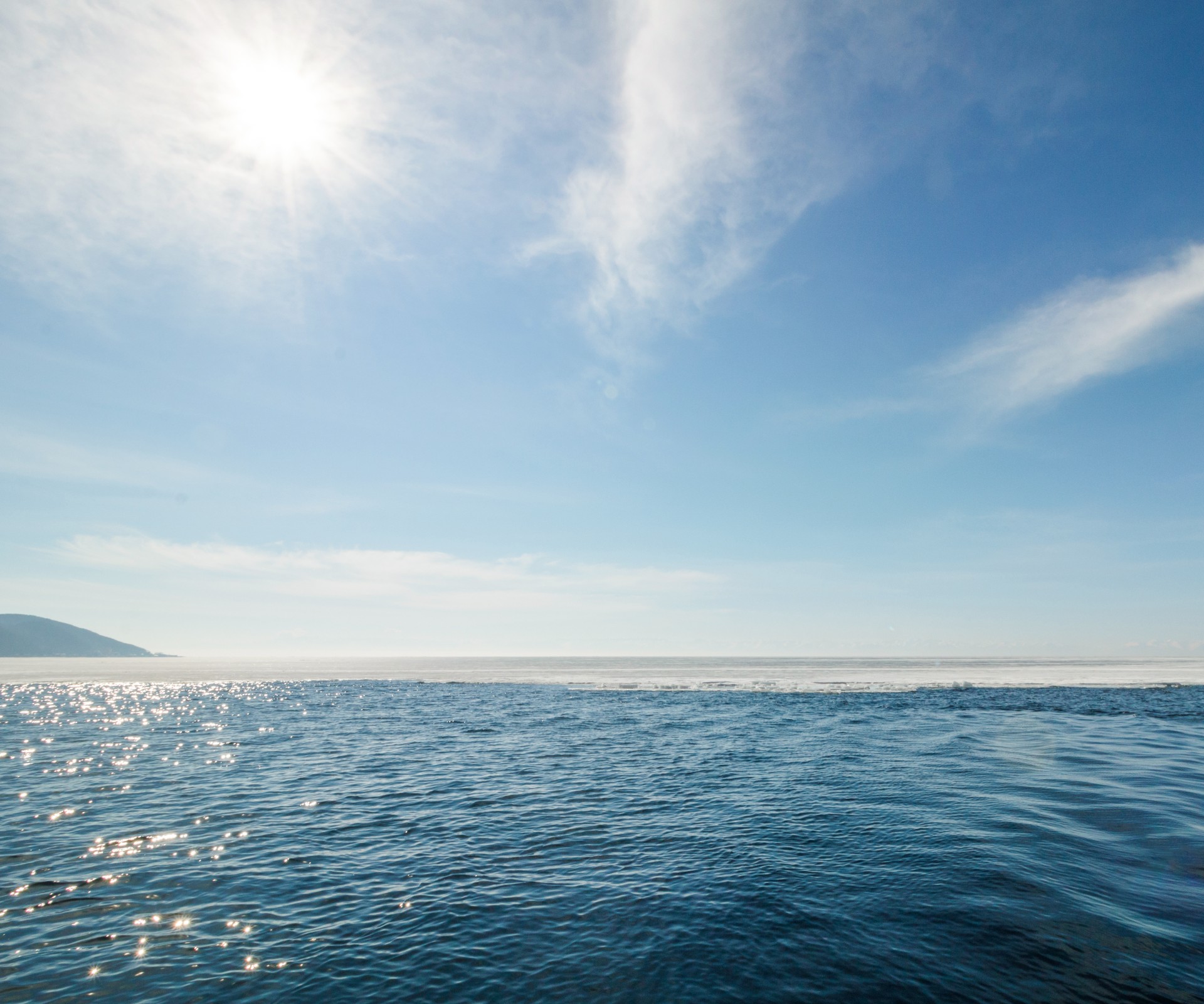 Weitblick auf das Meer mit Sonnenreflexionen und blauem Himmel mit leichten Schleierwolken